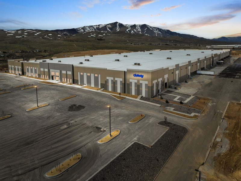 Aeriel view of the Reno Logistics Center development that is currently fully leased by the company Chewy. Their dark blue logo is placed on the building with lighting behind it.