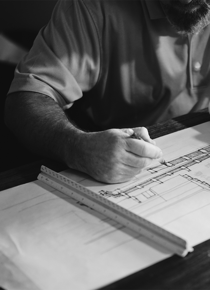 Man developing building plans. He is sitting at a desk with a pencil in his right hand.